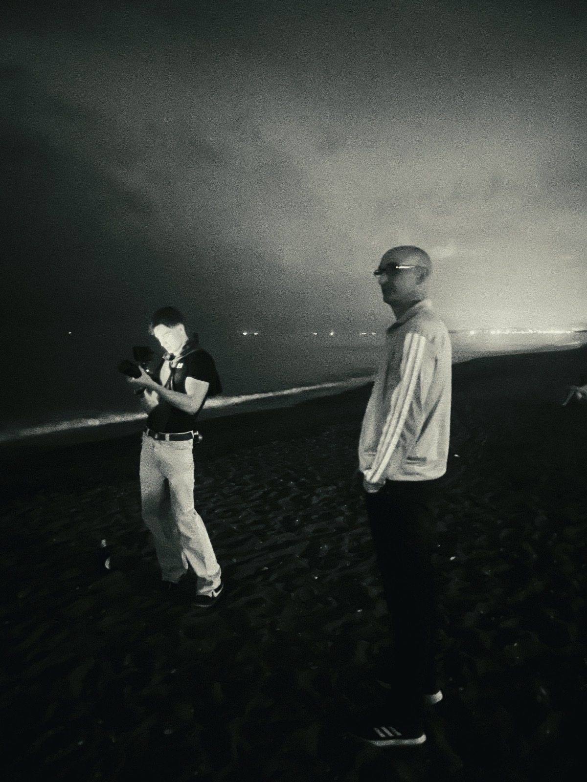 Black and white photo of Timon checking his camera on a beach at night