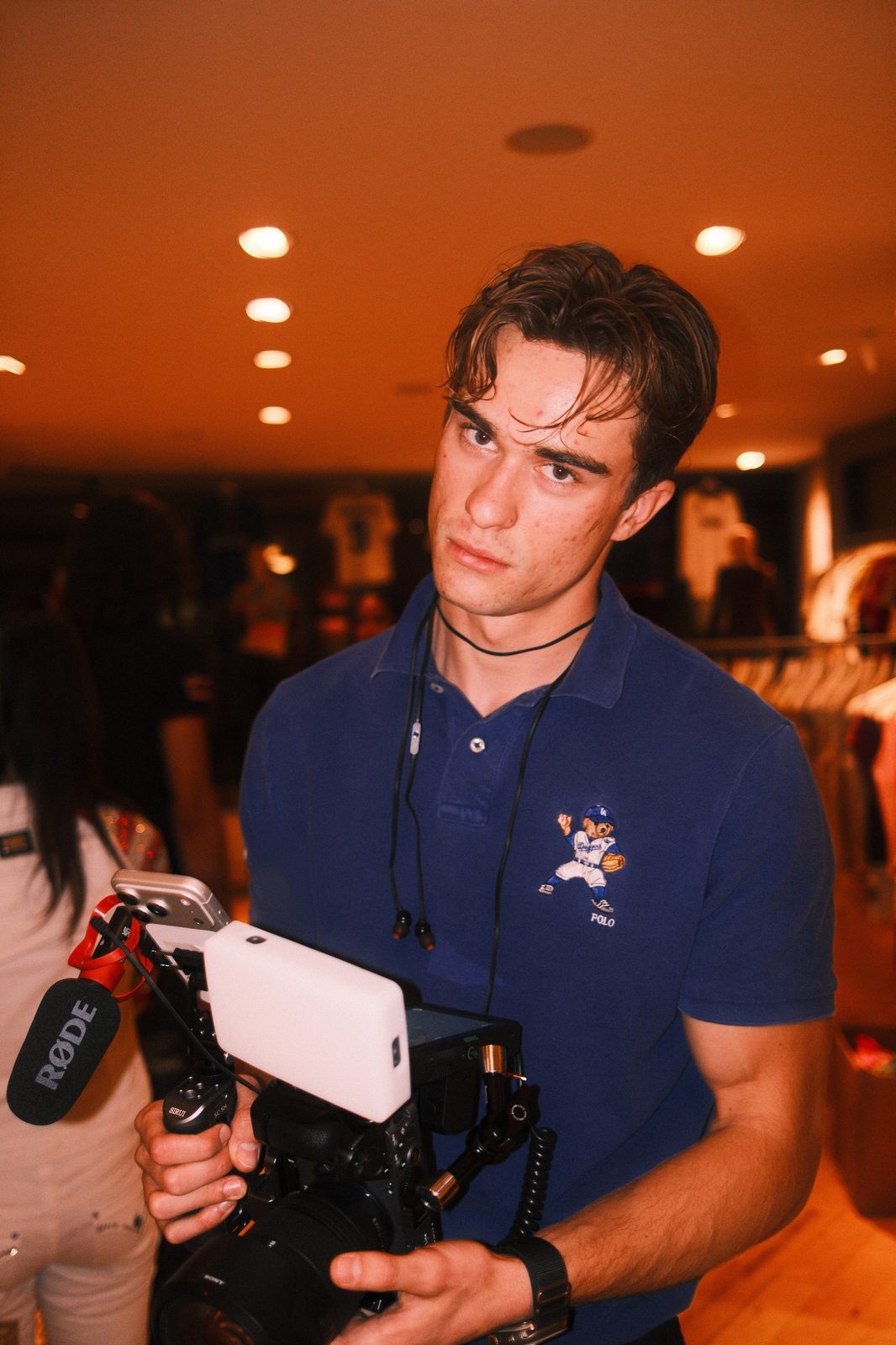 Timon in a blue polo shirt holding a Sony camera rig with a Røde microphone